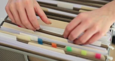 Kadın sekreter şirket arşivindeki klasörlerde belge arıyor. Kadın, kurumsal faturaları kontrol etmek için gerekli belgeleri içeren verilerle çalışıyor