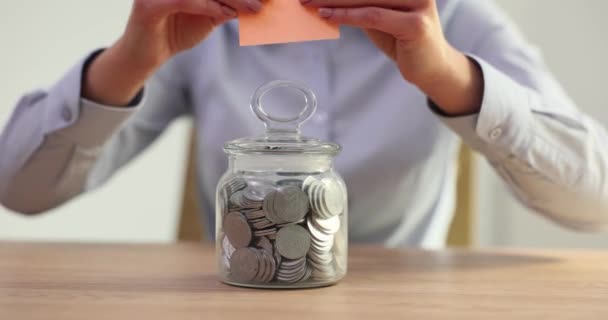女人把贴有字的贴纸放在桌上放着硬币的玻璃瓶上 夫人为未来的退休基金概念存钱 — 图库视频影像