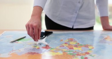 Kadın, dünya haritasında olası uçuş rotasını takip eden uçak modelini hareket ettiriyor. Bayan bir sonraki yolculukta minyatür uçak planlamasına rehberlik edecek.
