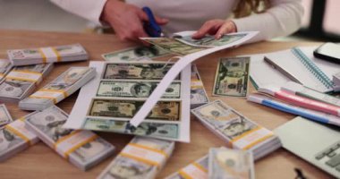 Kadın kalpazan, dolaptaki masada oturan sahte baskılı parayı makasla kesiyor. Sahte dolar banknotları. Ofiste ağır çekimde ödeme için uydurma.
