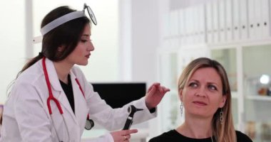 Kadın doktor, kadın hastaların kulak kanallarını büyüteç otoskop kullanarak inceliyor. Klinikte ağır çekimde olan hastanın profesyonel kontrolü
