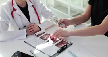 Kadın hasta, hizmetleri için minnettarlık göstergesi olarak doktor dosyasına para koyar. Kadın hastaneye ağır çekimde gayri resmi ödeme yapıyor.