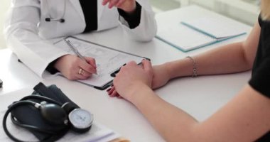 Doktor hastanın eline destek vererek tıbbi kayıtlar tutuyor. Klinikteki teşhisten sonra profesyonel kadın sakinleşir.