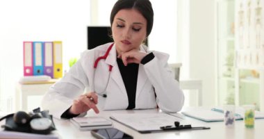 Steteskoplu kadın doktor randevulardan sonra ofiste oturarak para sayıyor. Bayan mali belgelerle çalışan hesap makinesi kullanıyor