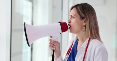 Kadın doktor hastane koridorunda dikilirken daha sesli konuşur. Bayan terapist hastalara önemli duyurular yapmak için hoparlör tutuyor.