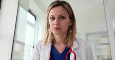 Ciddi yüzlü dikkatli kadın doktor yavaş çekimde kameraya doğru eğiliyor. Eldivenli sarışın doktor, profesyonel davranışlı kameraya poz veriyor.