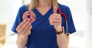 Kadın doktor donutu parmaklarıyla serin bir jest yapıyor. Kadın hekim, sağlıklı beslenmenin genel refahı artırmasının önemini vurguladı