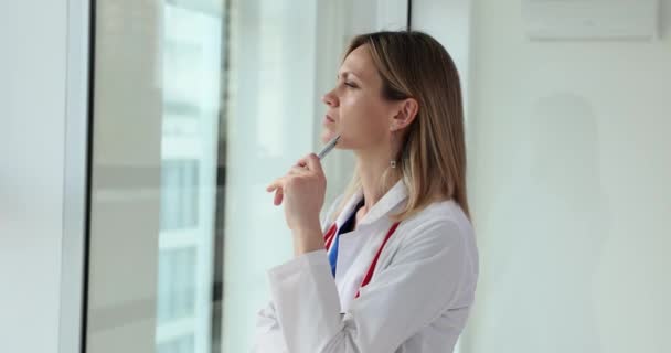 集中した女性医師は クリニックのゆっくりとした動きの広々とした窓の近くに立っています 休憩中の複雑な診断に対する女性の専門家の疑問 — ストック動画