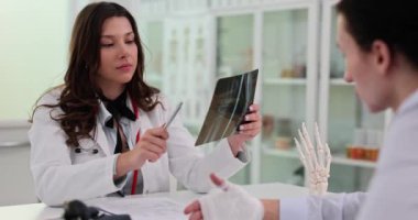 Kadın doktor kol röntgeni sonuçlarını açıklıyor. Bayan, endişe verici alanlara ya da dikkat çekici gözlemlere işaret eden görüntüleri yorumlar