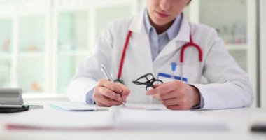 Doktor hasta için tıbbi reçeteyi dikkatlice kontrol edip imzalar ve pul yapıştırır. Sağlık sigortası belgeleri ve ödemelerin hazırlanması