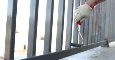 Metal bir çiti tekerlekle griye boyamak. Metal bir balkon ya da teras boyamak