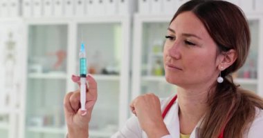 Kadın doktor ya da bilim adamı elinde mavi sıvıyla şırıngayı tutuyor ve inceliyor. Aşı ve insanları aşılama kuralları