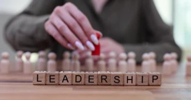 Tahta bloklar ve aynı beyaz şekiller arasında duran kırmızı şekilli liderlik kelimesi. Başarılı bir kariyer ve iş dünyasında liderlik becerileri.