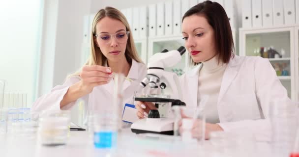 两名在实验室工作的女科学家 实验室助理正在把液体滴在实验室显微镜的玻璃上 有毒和有毒液体的研究 — 图库视频影像