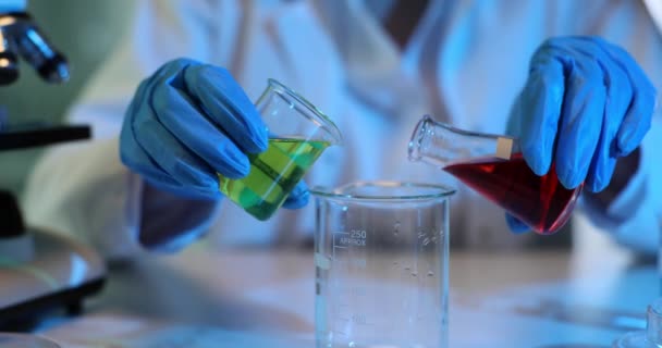 科学者は慎重にグリーンと赤い液体をガラスビーカーで混合し 実験室で実験を行っている 有毒で有毒な液体と混合物の研究 — ストック動画