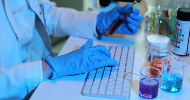 Naukowiec Niebieskich Rękawiczkach Używa Komputera Laboratorium Posiada Probówkę Krwią Lub — Wideo stockowe