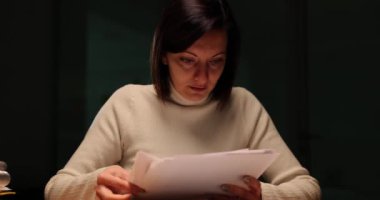 Genç bir kadın faturalara ve belgelere bakıyor ve geceleri ofiste stresli ve depresif hissediyor. Muhasebeci ya da patron mali borçları olan iş belgelerini inceliyor.