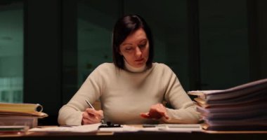 Yorgun kadın çalışanlar evrak işleriyle çok meşguller ve gece ofiste akıllı telefonlara bakıyorlar. Muhasebeci masada çok sayıda belgeyle oturuyor.