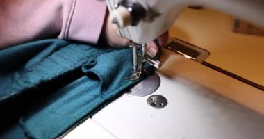 Profesyonel terzi dikiş makinesi kullanarak pantolon tamir eder. Pantolonları ve dikiş makinesindeki dikişleri onar
