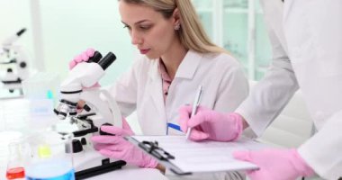 Bir meslektaşı test sonuçlarını yazarken bilimsel araştırmalar ve kadın bir bilim adamı mikroskoba bakıyor. Bilimsel tıbbi ve biyolojik deneyler