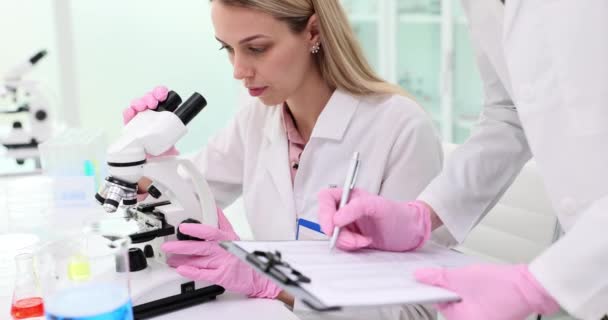 Badania Naukowe Kobieta Naukowiec Patrzą Mikroskop Podczas Gdy Kolega Zapisuje — Wideo stockowe