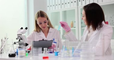 Laboratuvarda çalışan iki kadın bilim adamı mavi bir sıvıyla dolu bir test tüpünden elde edilen sonuçlardan memnunlar.
