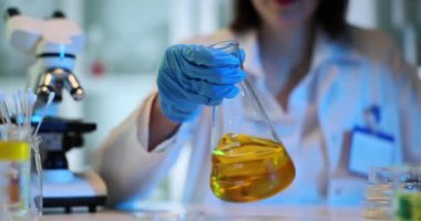 Eldivendeki bilim adamları steril şişeyi sarı sıvıyla tutuyorlar. Laboratuvarda petrol ürünlerinin test edilmesi