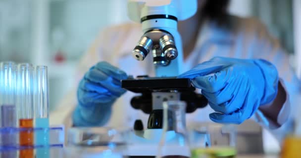 近代的な実験室装置を使用した新素材の顕微鏡解析 青い手袋の研究者は顕微鏡のスライドのサンプルを注意深く置きます — ストック動画