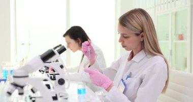 Sarışın öğrenci reaksiyon için pipetle birlikte sıvıyı konteynıra atar. Bilim adamı, yavaş çekim yayılmasını önlemek için ölçümlerde doğruluğu garanti altına alıyor