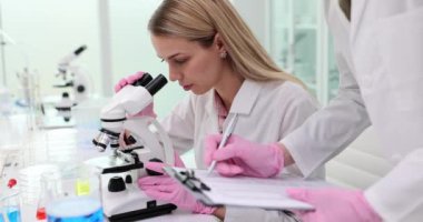 Bayan laboratuvar asistanı mikroskopla çalışan meslektaşından bilgi alıyor. Bilim adamları verileri gerçek zamanlı olarak yakalayarak doğruluğu yavaş çekimde sağlıyorlar.