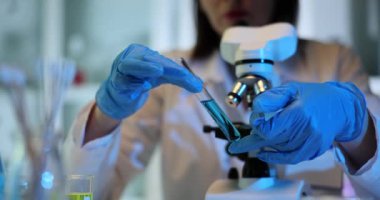 Araştırmacı laboratuarda test tüpünü mikroskoba karşı hareket ettiriyor. Profesyonel bir kadın, değerli verileri yavaş çekimde toplamak için kapsamlı bir analiz yapar.