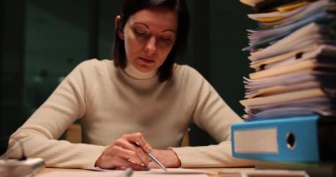 Yorgun bir kadın akşam ağır çekimde ofiste çalışmak için son teslim tarihlerine yetişmeye çalışır. Bayan yorgunluğunu ifade eden klasörlerle başını masaya koyar.