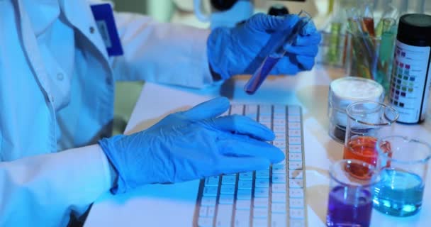Pracownik Laboratoryjny Rękawiczkach Posiada Probówkę Próbką Wpisującą Dane Klawiaturze Asystent — Wideo stockowe