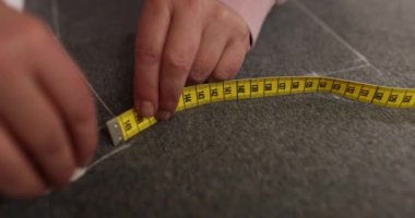 Terzi kumaş üzerindeki kesin çizgileri işaretlemek için tebeşir ve ölçüm aracı kullanır. Kadın, giysinin her bölümü için doğru boyutları garanti ediyor