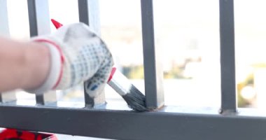 Bir işçinin elleriyle metal bir çiti boyamak. Çiti gri bir fırçayla boyuyorum..