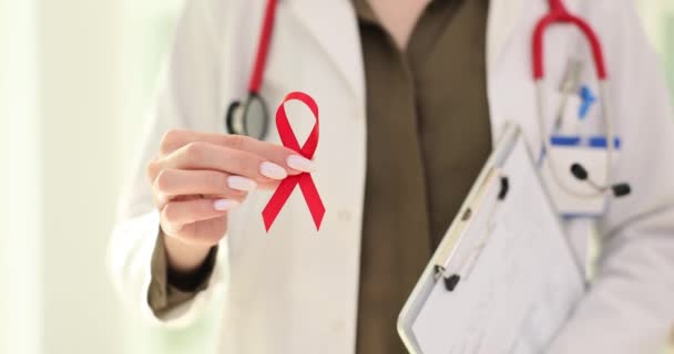 クリニックで赤いリボンを抱えている医師 セラピストはエイズのシンボルとして病院で赤いリボンを保持しています — ストック動画