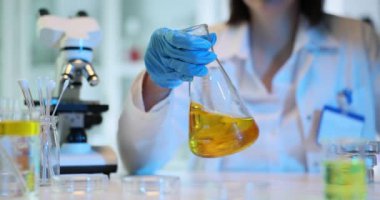 Bilim adamı biyolog temiz sarı bir sıvıyla eğimli cam bir şişe tutuyor. Petrol araştırması ve zehirli sıvı kavramı