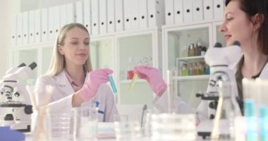 Farklı renkte test tüpleri olan iki kimyager ve laboratuvarda başarılı bir deney. İki laboratuvar teknisyeni arasında başarılı bir işbirliği.