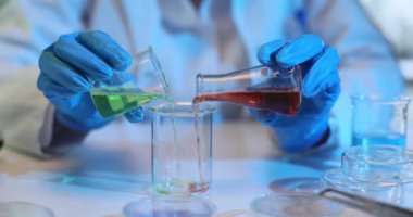 Bilim adamı kimyager laboratuvar üzerinde deney yapıyor ve renkli sıvıları karıştırıyor. Laboratuvar teknisyeni iki sıvıyı dikkatlice karıştırıyor, yeşil ve kırmızı, cam bir şişede.