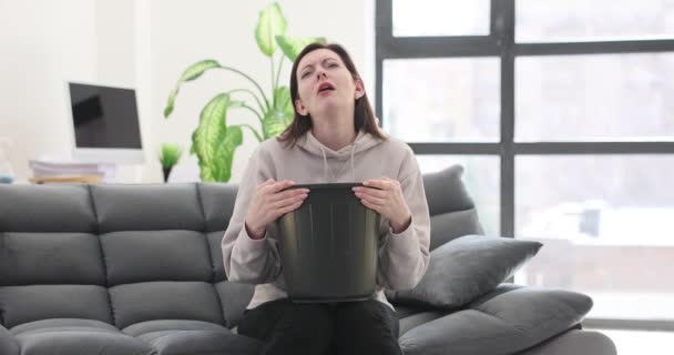 若い女性はゴミ箱に頭が付いているソファーに座ります 吐き気 健康と毒性の低下 — ストック動画
