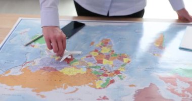 İşadamı haritanın yüzeyinde minyatür bir uçağı hareket ettirir. Haritayı dikkatle inceleyen insan, farklı rotalar ve yavaş çekim güzergahları planlar.