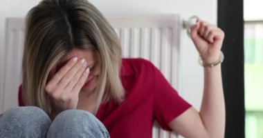 Korkmuş genç bir kadın radyatöre kelepçeli bir şekilde yerde oturup ağlar. Aile içi şiddetin çaresiz kadın kurbanı yardım arıyor
