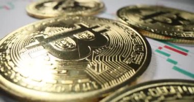Altın bitcoin koleksiyonu masanın üzerinde jeton fiyat grafikleriyle birlikte kağıtların üzerinde bulunur. Sikkeler dünyadaki değerli dijital para birimini sembolize eder.