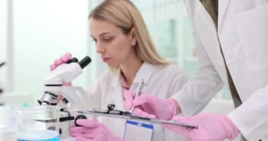 Sarışın kadın kimyager laboratuarda mikroskop ile numuneleri inceliyor. Analiz sonuçları yavaş çekim kontrolünde.