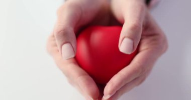 Kadın, ellerinde kalp minyatür modelini gösteriyor. Genç bayan, kalp şeklinde elleri olan bir oyuncağın sıcaklığını ve sevgisini taşıyor.