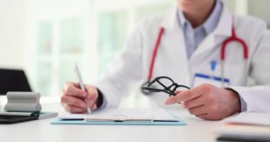 Doktor hastaya reçete yazar ve gözlük tutar. Terapist tıbbi belgeleri dolduruyor.