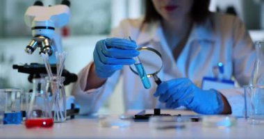 Bilim adamı mavi sıvı örneğini büyüteçle inceliyor. Zehirli sıvının tüp bebek üzerinde çalışması