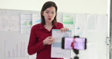 Businesswoman analyzes financial data and statistics recording an educational video for blog. Marketing manager blogger records video on a smartphone for subscribers