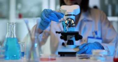 Bilim adamları mikroskobun arka planında mavi sıvıyla test tüpünü tutuyor ve inceliyor. Zehirli sıvıların modern laboratuvar ve kimyasal araştırmaları