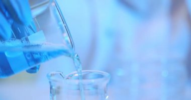 Mavi sıvı mataraya dökülüyor. Bilim adamı araştırmacı laboratuvar asistanı mavi kimyasal sıvıyı inceliyor.